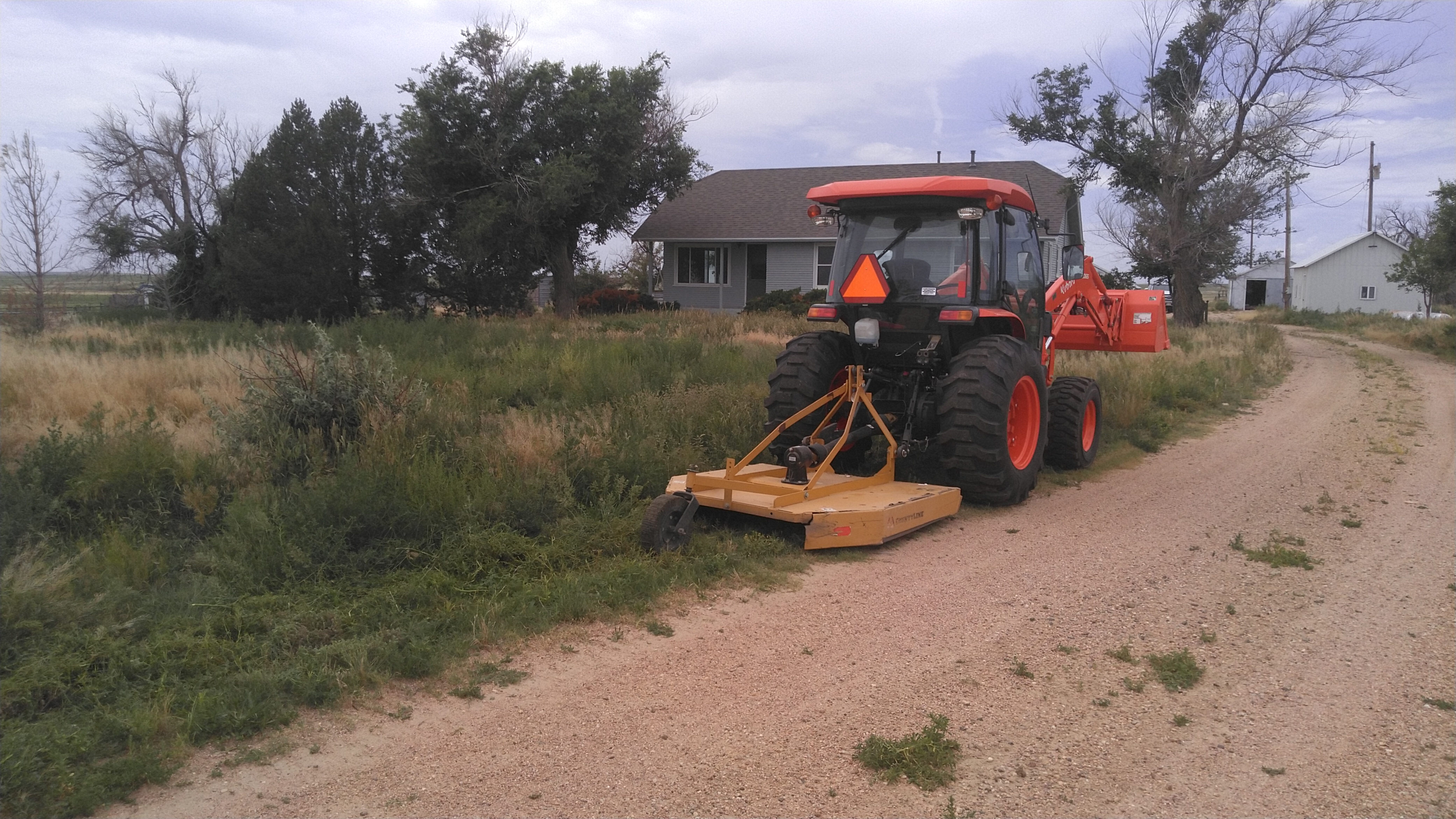Tractor with brush hog mower attachment cutting overgrown grass and weeds on a rural Colorado property