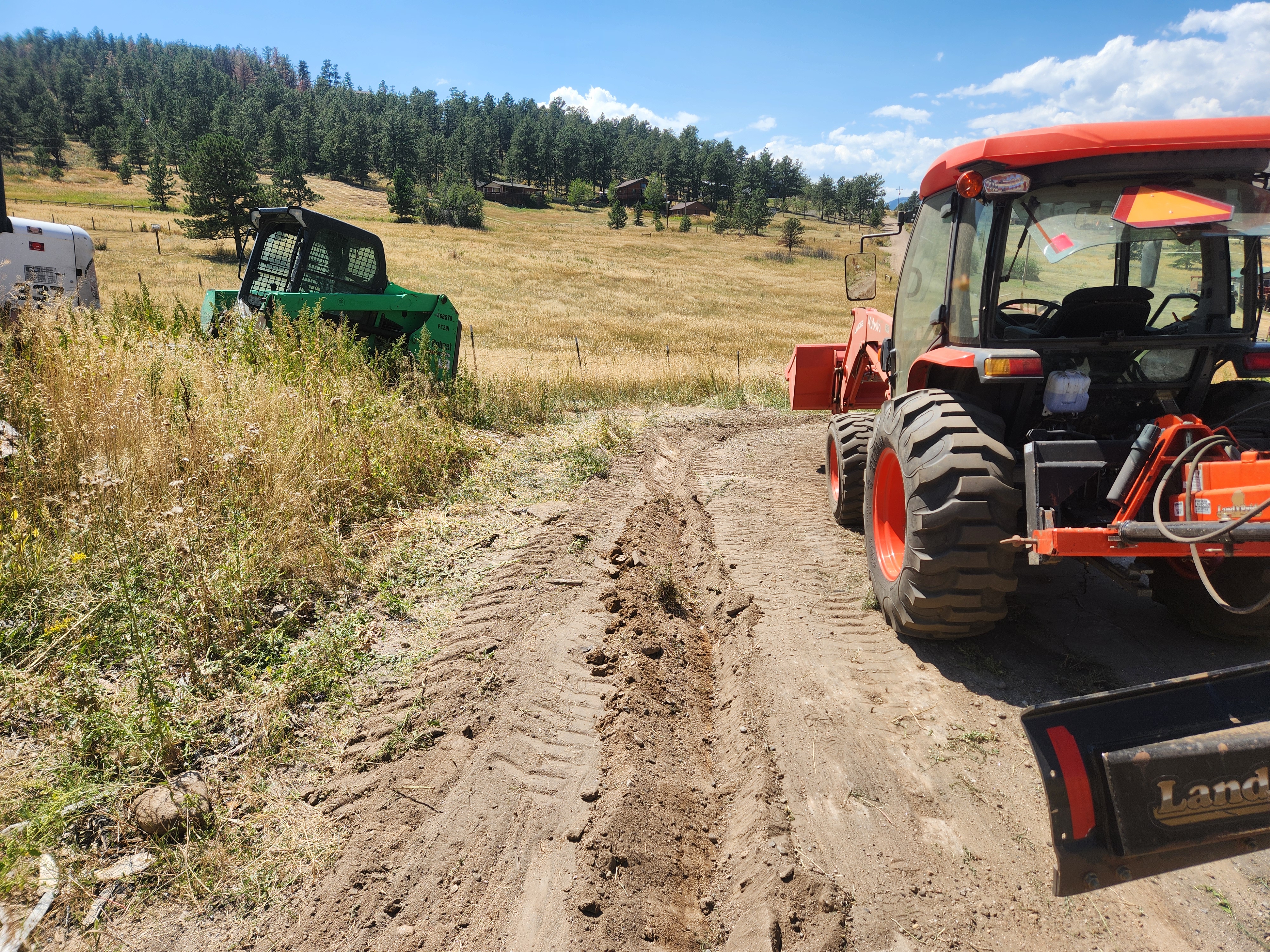 Rough, rutted dirt driveway before grading — tractor on site ready to work