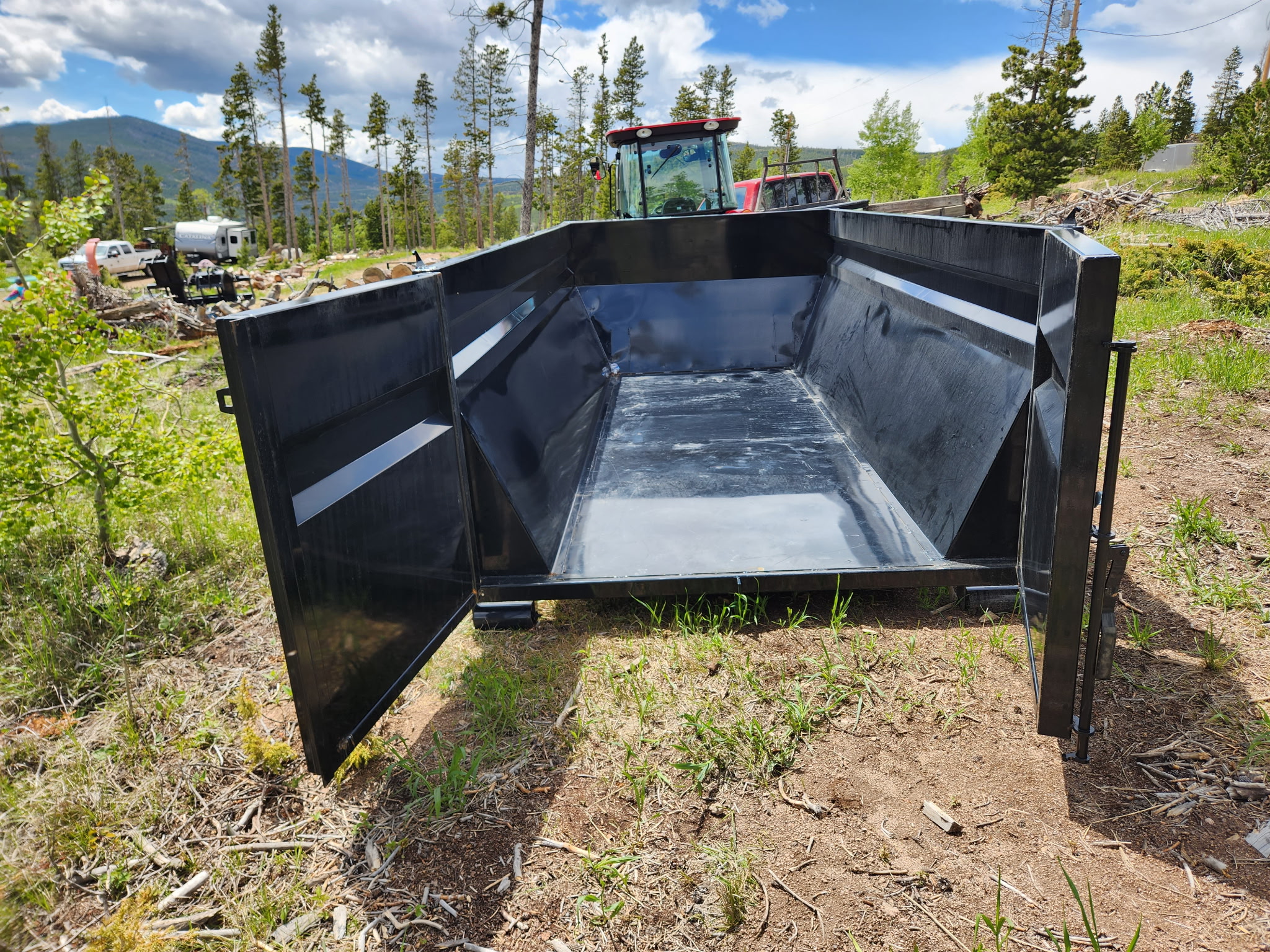 14 cubic yard black dumpster with doors open on a Colorado mountain property with tractor in background