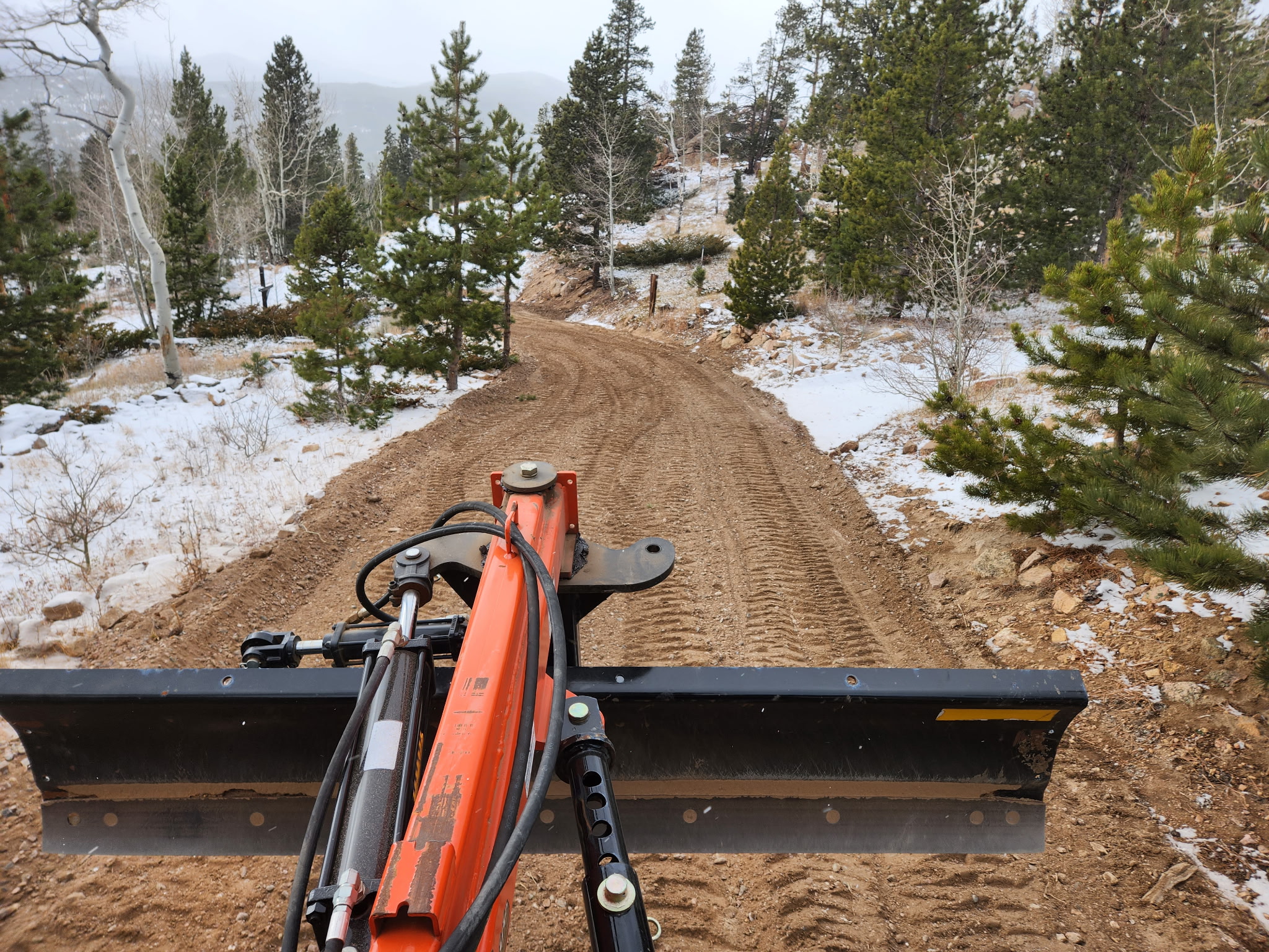 Freshly graded road through snowy Colorado pines — view from behind the tractor blade